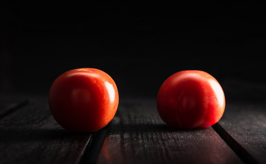 Two illuminated and isolated red tomatoes on dark wooden table and  black background. Bio and raw tomatoes from garden shining on wooden board, spotlighted with natural light from side.