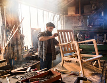 A Craftsman In His Workshop Working On An Armchair Frame 