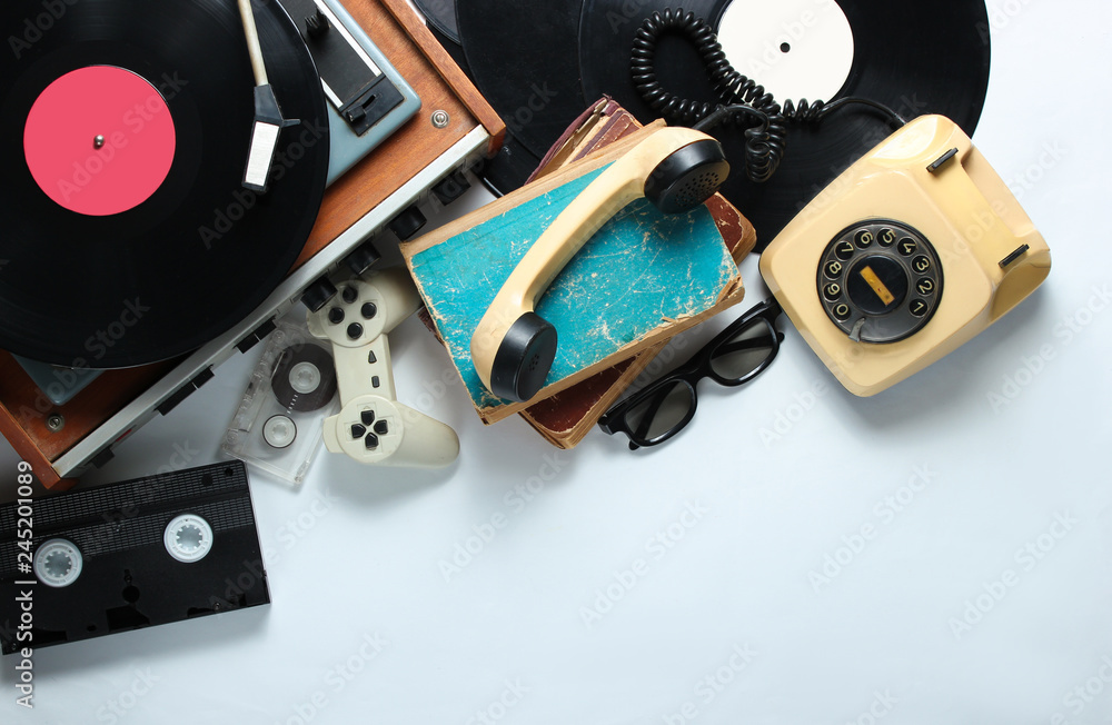 Retro 80s pop culture objects on white background. Copy space. Rotary phone, vinyl player, old books, audio, video tapes, 3d glasses, gamepad. Top view. - obrazy, fototapety, plakaty 