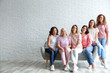 Group of women with silk ribbons on sofa against brick wall, space for text. Breast cancer awareness concept