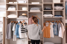 Woman Choosing Outfit From Large Wardrobe Closet With Stylish Clothes And Home Stuff