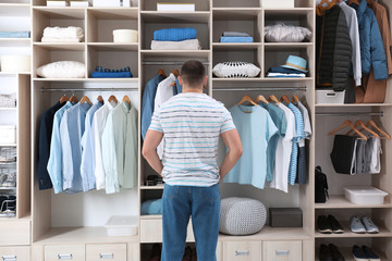 Canvas Print - Man choosing outfit from large wardrobe closet with stylish clothes, shoes and home stuff