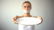 Skinny woman with taped mouth showing empty plate, concept of fasting, hunger