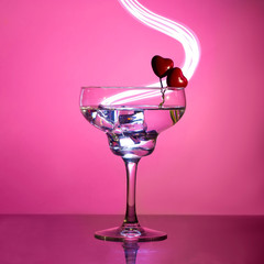 glass with a cocktail and two hearts. Valentine's day and wedding concept.