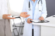 © rogerphoto - Unknown doctor and  female patient  discussing something while standing near reception desk in emergency hospital. Physician at work in clinic. Medicine and health care concept