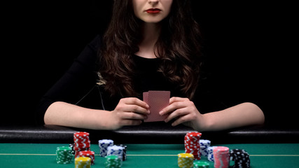 Woman player checking her cards combination, bluffing at casino poker game