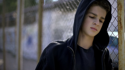 boy in hoodie leaning on fence, orphan in boarding school, confinement