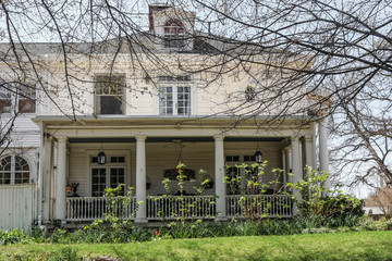 Wall Mural - Old stately but shabby wooden home in early spring with budding branches and flowers starting to grow up around it in disarray