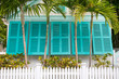 View of charming colorful window shutters framed by tropical palm trees and a white picket fence on a residential street in Key West, Florida, USA