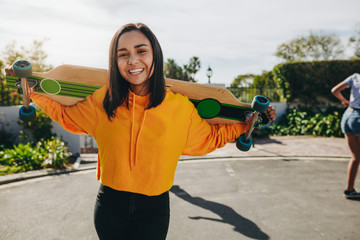 happy girl carrying a longboard on her shoulders