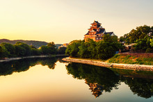 Castle In Okayama, Japan In The Morning With River And Colorful Yellow Sky At Sunrise