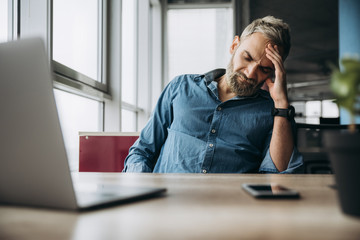 Exhaustion. Tired young man in stylish wear working with laptop while sitting in the office