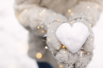 Wall Mural - Woman holding Christmas lights and heart made of snow, closeup