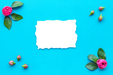 Wall Mural - Floral mockup. Flowers, petals, leaves around white paper on blue background top view copy space frame