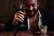 A man in his shirt unbuttoned is drinking sparkling wine from a glass.