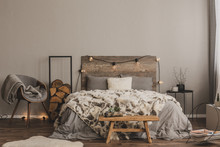 Stylish Grey Chair With Blanket And Log Of Wood Next To Warm Double Bed With Wooden Headboard And Light Bulbs