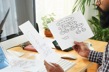 Programmer or software developer looking through papers with schemes containing information about decoding