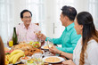 © DragonImages - Asian family having delicious meal and clinking with glasses at table on dinner spending time together