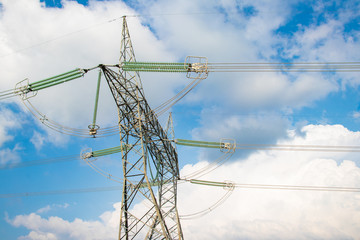 Electrical high volatge power line tower pillar on meadow hill area in front of blue sky and clouds