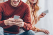 cropped shot of smiling man and young wife using smartphones at home, mistrust concept
