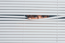 Suspicious Young Man Peeking And Looking At Camera Through Blinds, Mistrust Concept