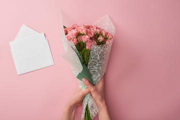 Sticker - cropped shot of woman holding bouquet of beautiful roses and white envelope isolated on pink