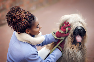 Wall Mural - African girl in a coat playing with a dog of the Briard breed on a city street on a winter day close-up.