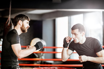 Wall Mural - Boxing trainer showing to a man how to fight, teaching to box in the boxing ring at the gym