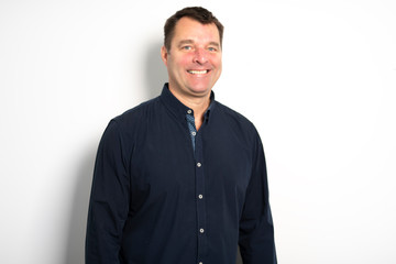 Head and shoulders portrait of a bearded middle-aged man looking thoughtfully at the camera over a white studio background with copy space