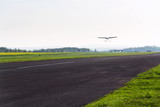 Fototapeta  - Unmanned aerial vehicle surveillance drone with light and camera landing on airport runway, ground, airfield, sunny summer morning, drone delivery concept, copy space on clear sky