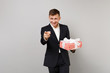 © ViDi Studio - Handsome business man pointing index finger, holding red striped present box with gift ribbon isolated on grey background. Achievement career wealth business. Valentine's Day birthday holiday concept.