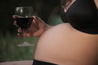 © agarianna - close up of pregnant woman belly, with hand holding red wine glass, outdoors
