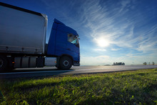 Blue Truck Driving On The Asphalt Road On A Horizon Against The Glowing Sun