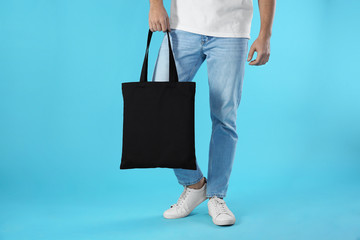 Wall Mural - Young man holding textile bag on color background, closeup. Mockup for design