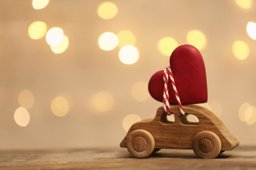 Toy car with red heart on table against blurred lights. Space for text