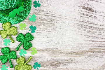 St Patricks Day side border of shamrocks with leprechaun hat over a rustic white wood background