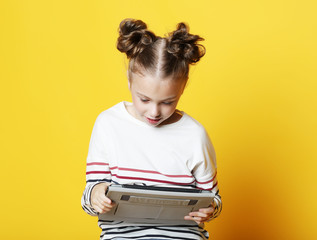 Wall Mural - Little girl with tablet on yellow studio background.