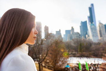 New York City Asian woman walking in winter in Central Park by the skating rink pensive looking at NYC skyline background. Urban city lifestyle living people outdoor.