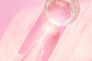 Top view of sparkling water in transparent glass and sun glare on pink background.