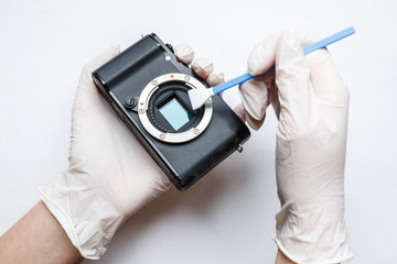 Close-up of mirrorless digital APS-C dirty camera matrix sensor cleaning and maintenance with swab, photographer cleaning photocamera on white background