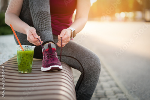 Green detox smoothie cup and woman lacing shoes before workout.
