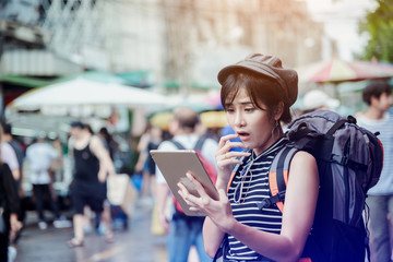 Young happy asian woman tourist in market shopping with tablet computer for online map.Traveling backpacker girl looking at city map on digital tablet outdoor .Travel tourism,technology concept.