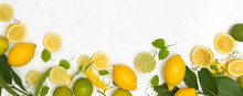 Many Fresh Lemons And Limes And Green Leaves On White Crumpled Paper Background