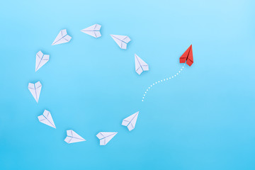 Wall Mural - Group of white paper planes fly in a circle and one red paper plane pointing in different way on blue background. Business for new ideas creativity, innovative and solution concept.