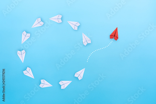 Group of white paper planes fly in a circle and one red paper plane pointing in different way on blue background Poster Mural XXL