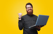 © Vulp - Cheerful bearded man is holding laptop and poiting bkack, looking at camera over yellow background