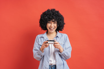 Excited casual young woman playing video games having fun on red background