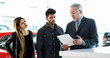 © Minerva Studio - Car dealer reading a contract to a couple in an auto showroom