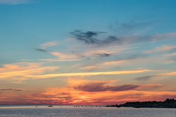 Wall Mural - Evening sunlight on coast, pink clouds, blue sky reflection on water. Beach in summer. Seaside natural environment. Shore in Harilaid, small island in Estonia. Nature Reserve in North Europe