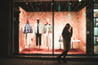 Portrait of a girl on the background of a fashion store showcase. Girl walks at the window of a fashion shop with dummies at night.
